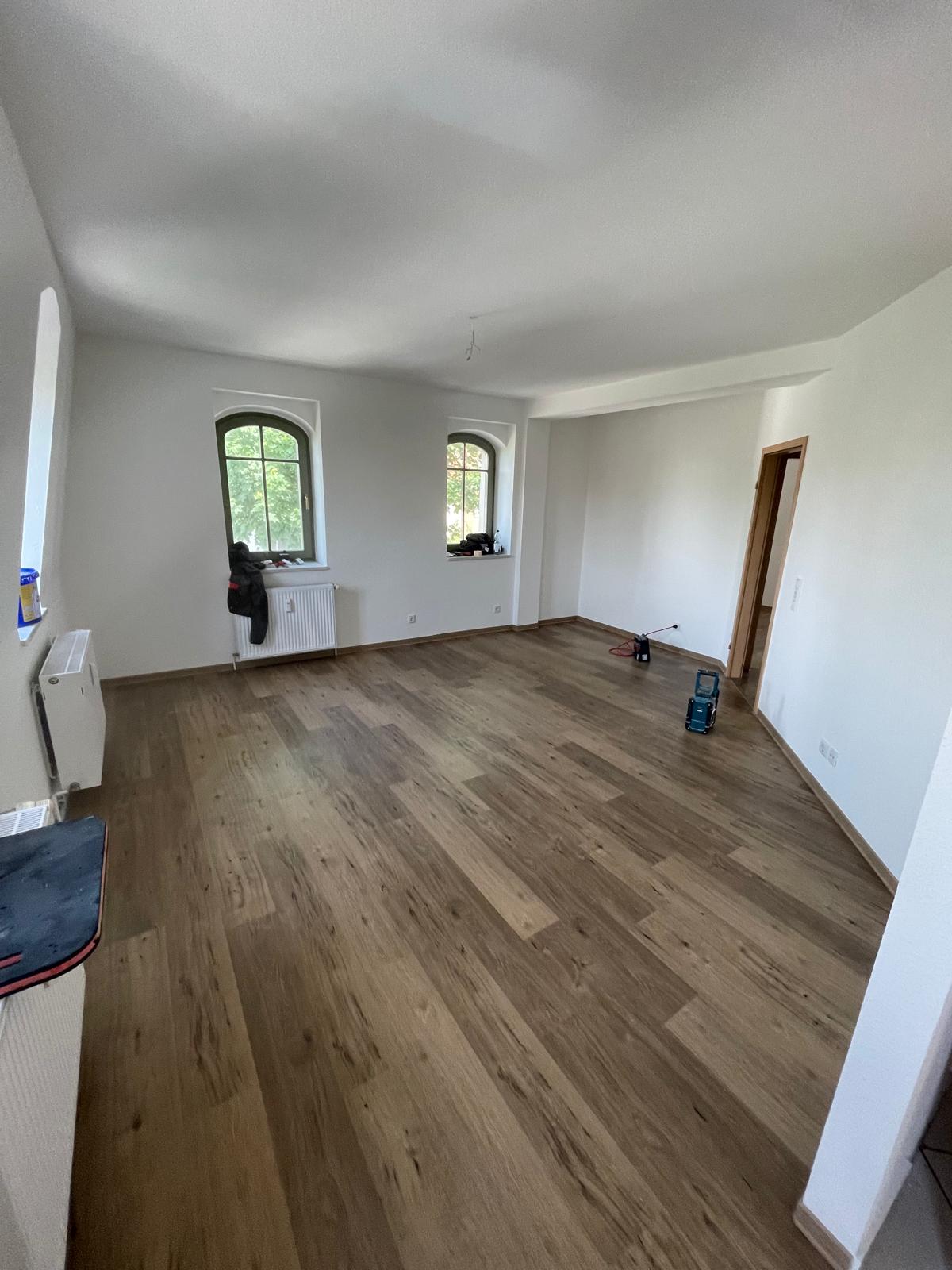 Heller Altbauwohnraum mit warmem Vinylboden und hohen Bogenfenstern